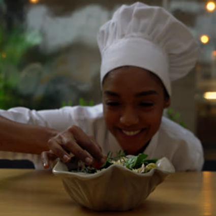 Beautiful black female chef adding a finishing touch to a salad while facing camera smiling very happy